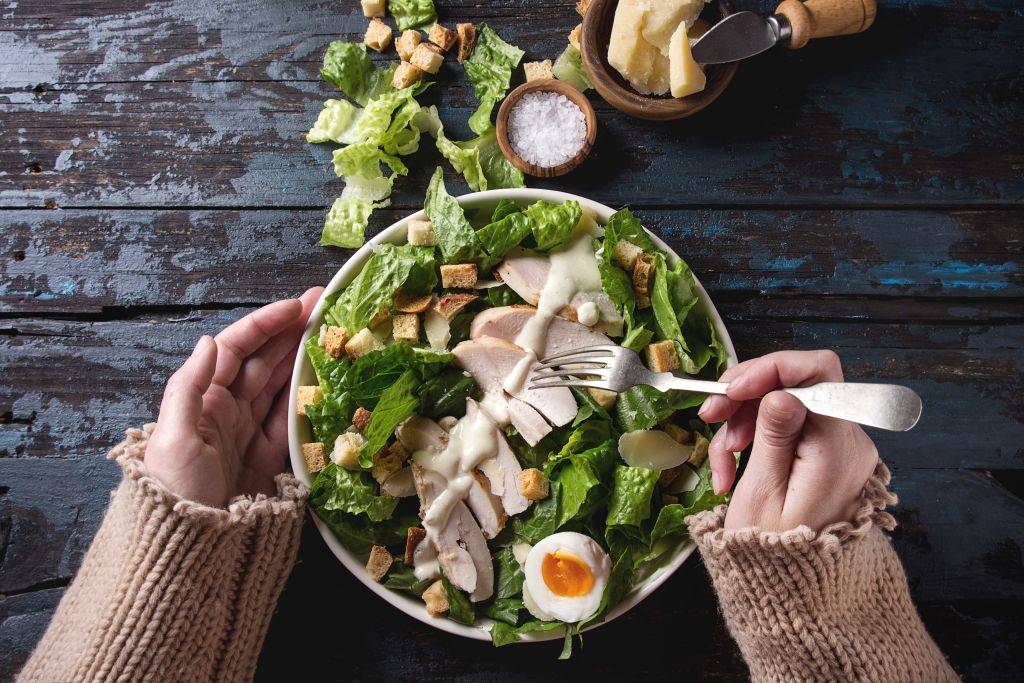 Female hands take by fork Classic Caesar salad with chicken breast in white ceramic plate
