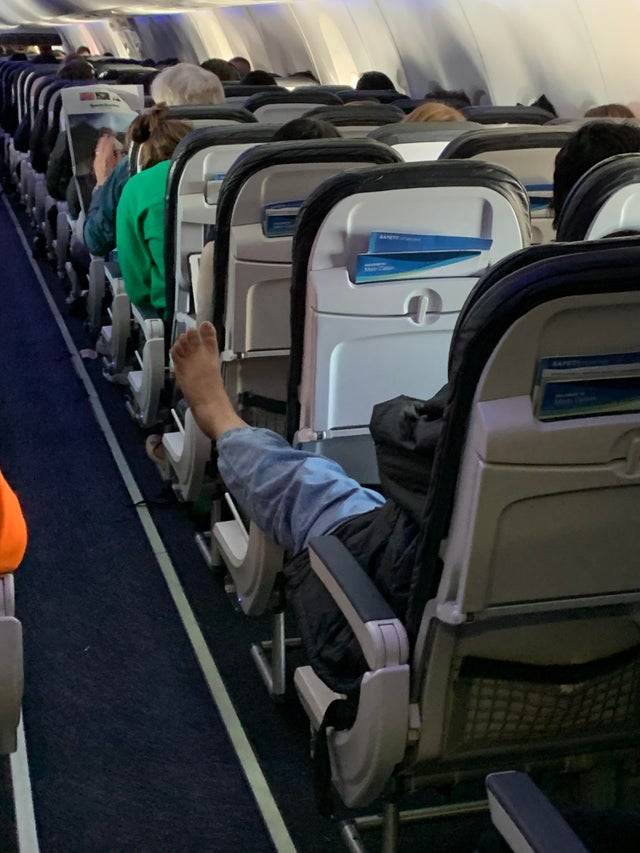 Barefoot person on plane stretching feet out in aisle