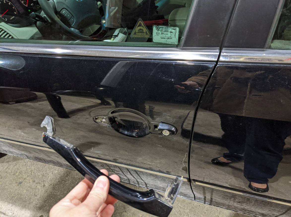 A woman holds the handle of her car door which has just broken off.