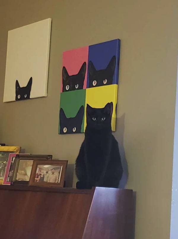 Black cat blending in with cat painting on the wall.