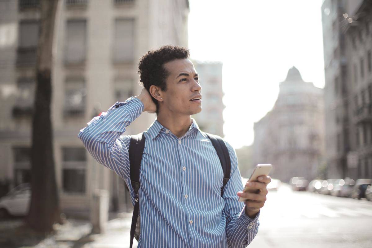 Man outside holding cell phone looking up confused