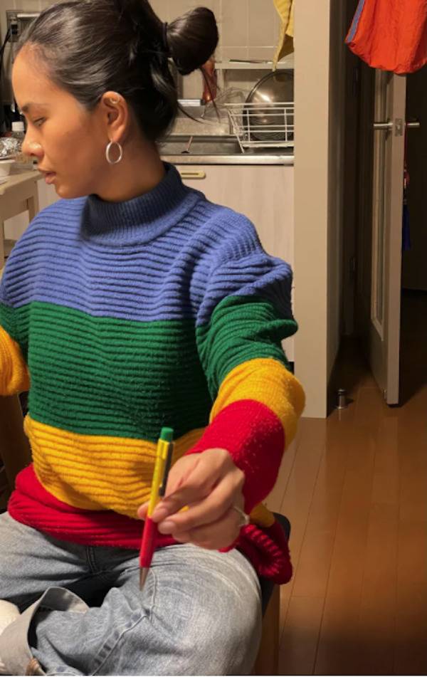 Woman holding a multi-colored pen that blends into her multi-colored sweatshirt.