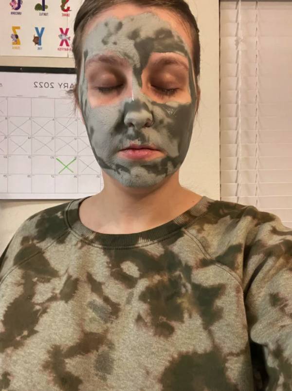 Woman wearing a green and grey sweatshirt and a green and grey face mask.