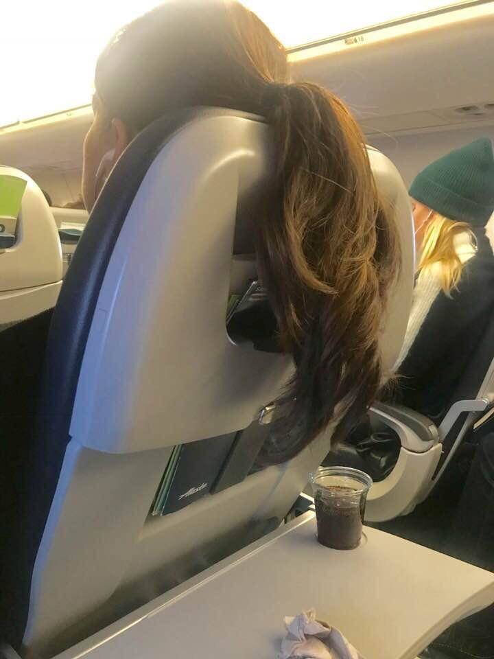 Woman on airplane has hair thrown over seat back into next row