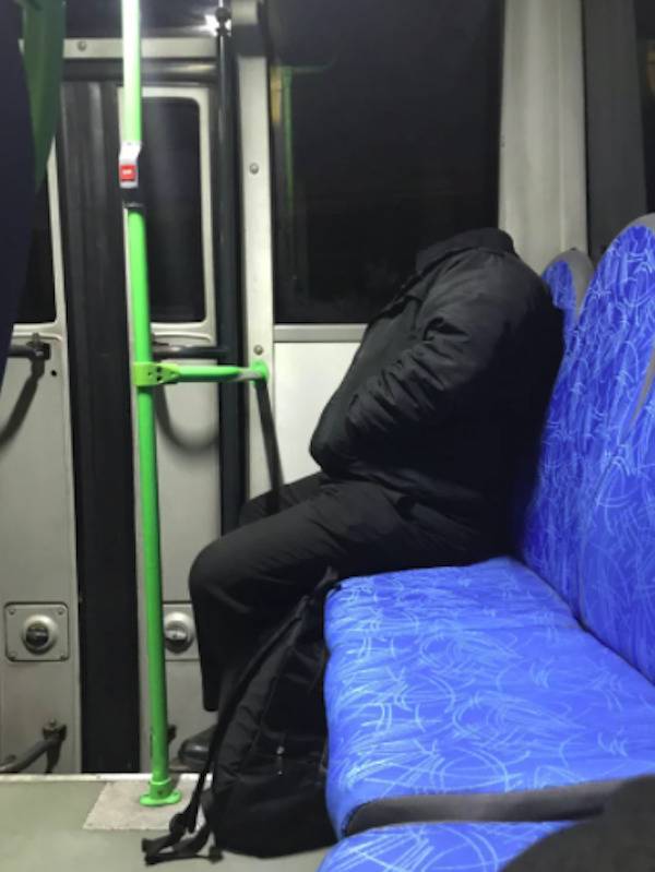 Man in all black sitting on a bus and the shadow makes him look headless.