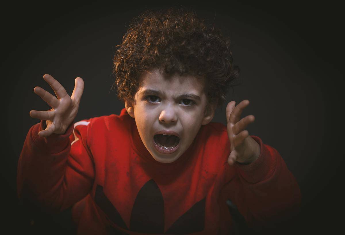 A boy in a red shirt looks angrily at the camera.
