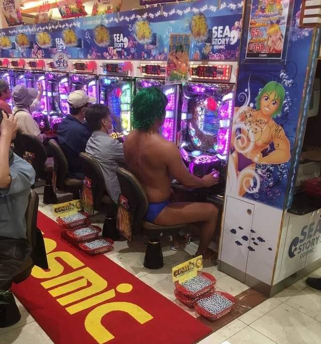 Man wearing speedo with green hair sits at merman slot machine