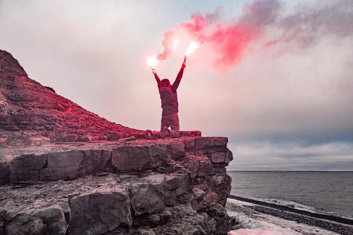 Man holding red flares on rock face