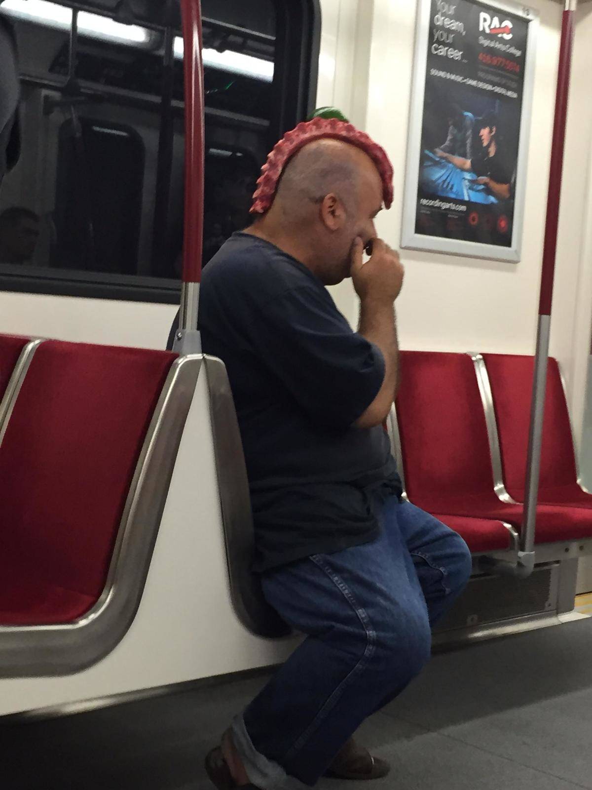Man riding city subway has raw meat that appear to be ribs or a spine on his head as a mohawk 