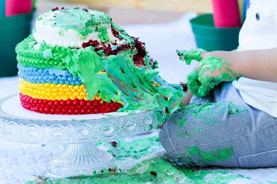 A colorful birthday cake has been smashed by a little boy.