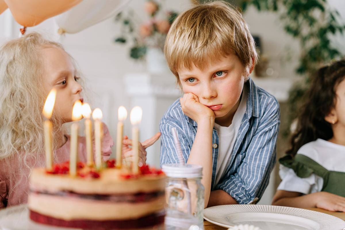 A boy looks sadly at a lit birthday cake.