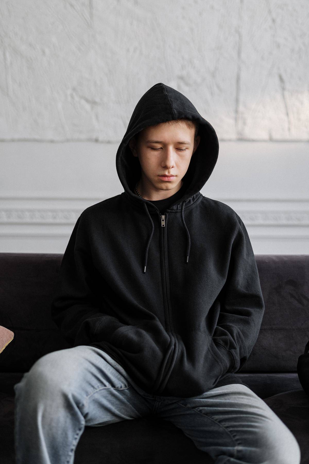 Teen wearing black hoodie looking downcast on couch