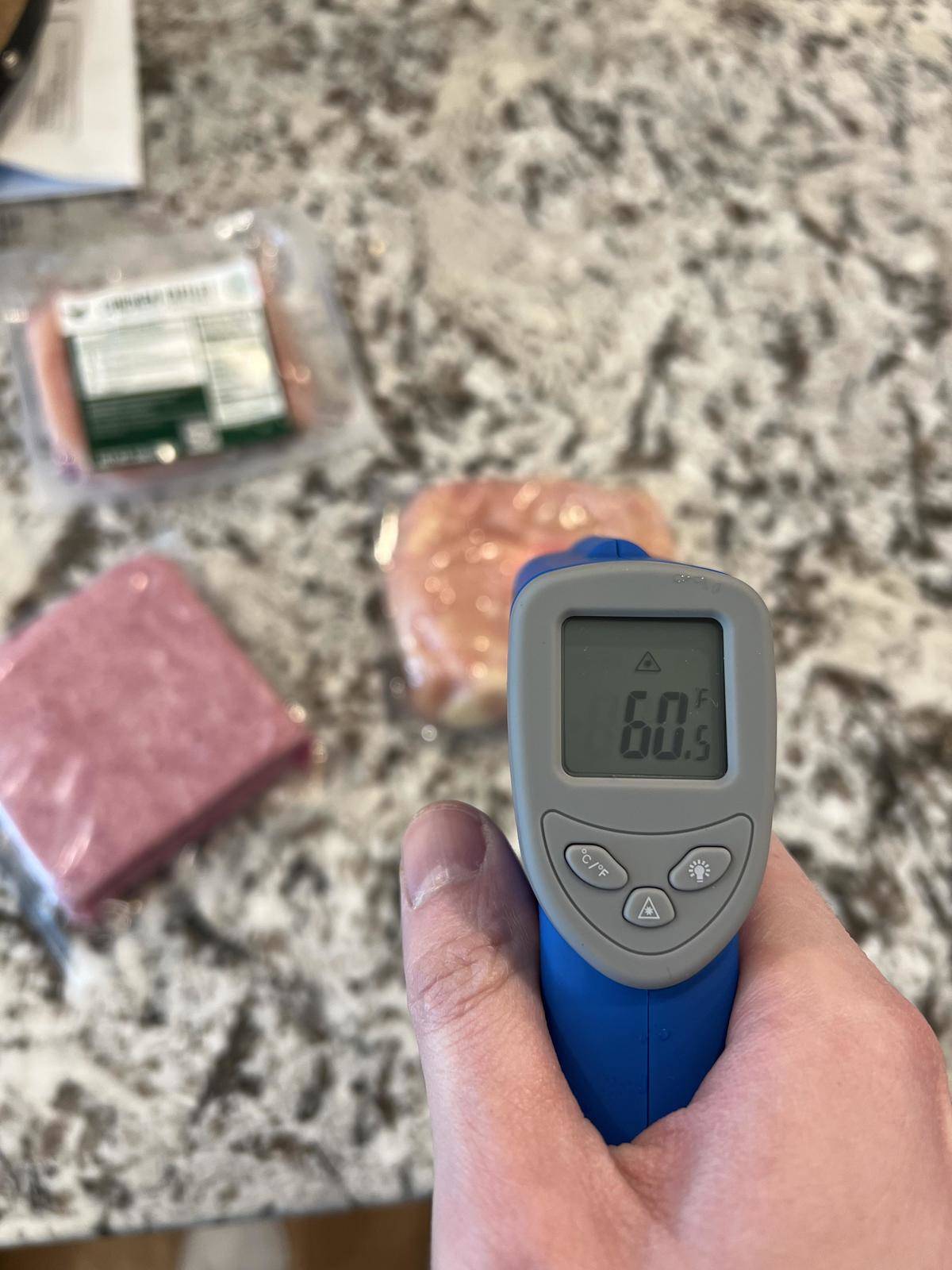 A digital thermometer reads the temperature of packaged meat at 60.5 degrees F.