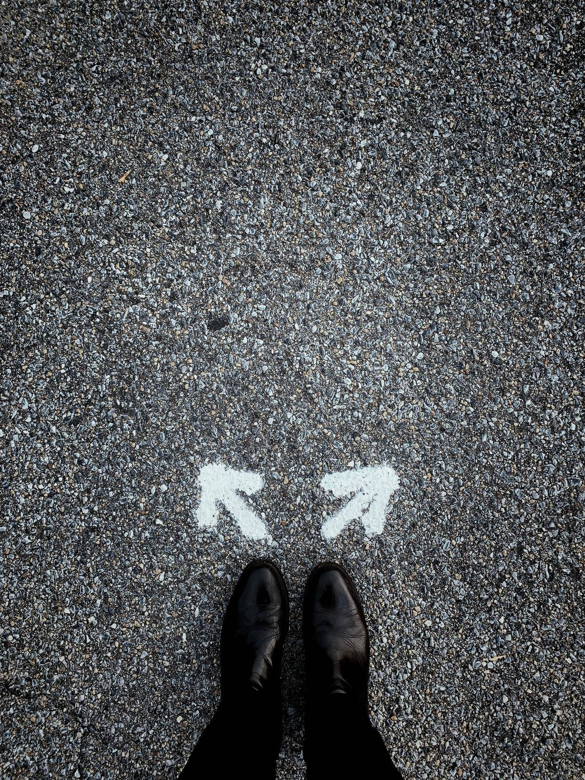 Black boots with two arrows drawn on the ground in chalk leading different ways