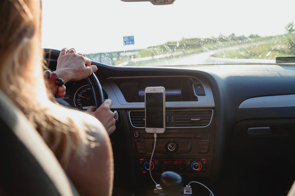 Woman driving car with phone on dashboard 