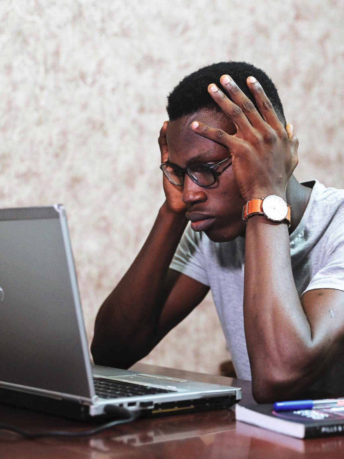Man with two hands on his head looking at a laptop. 