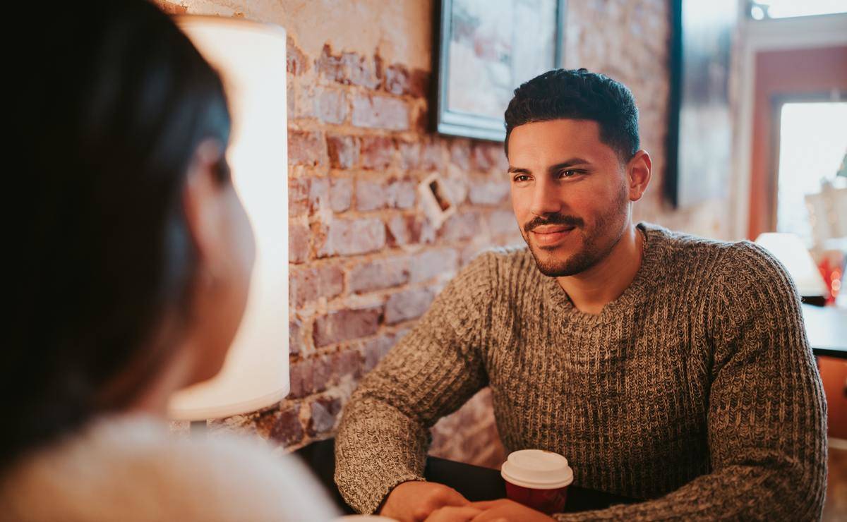 Man holding coffee smiles across table at woman 