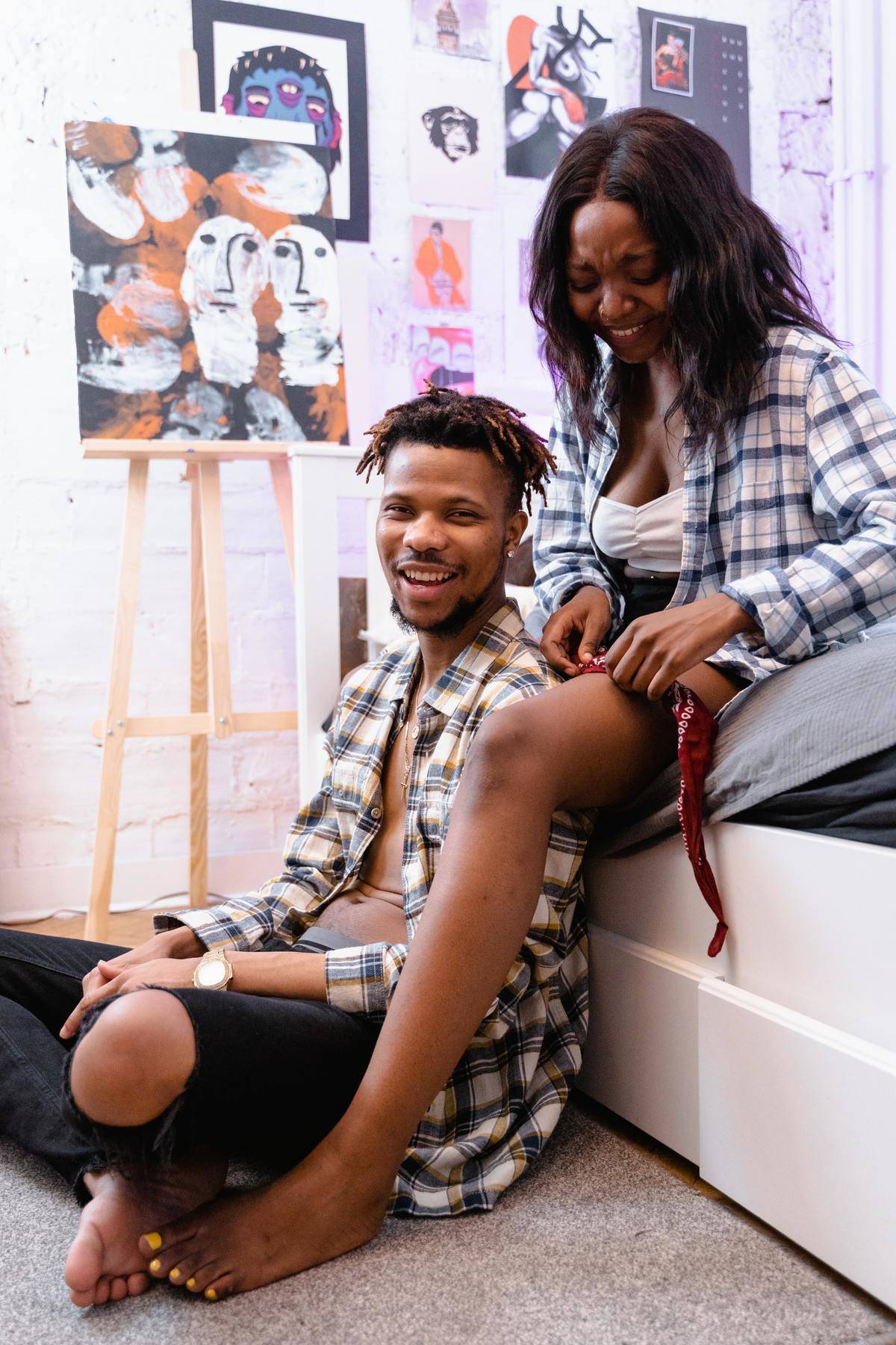 Man and woman laughing seated on floor with artwork behind them