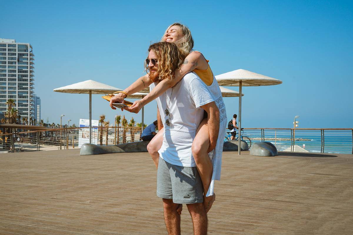 Man giving woman piggyback ride while walking outside near beach laughing