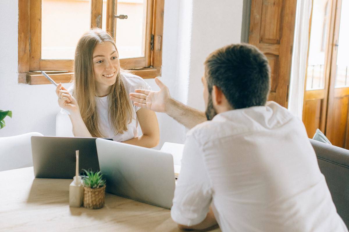 Man and woman talking across laptops man's hand outstretched woman smiling 