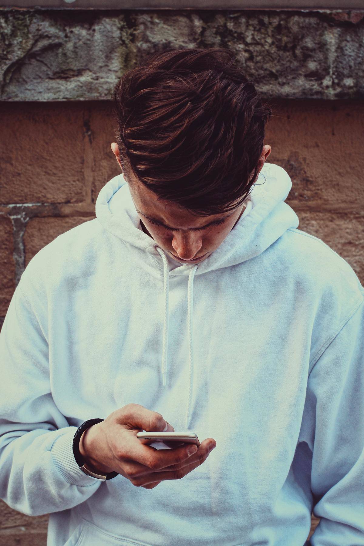 Young man in white hoodie looks down at cell phone