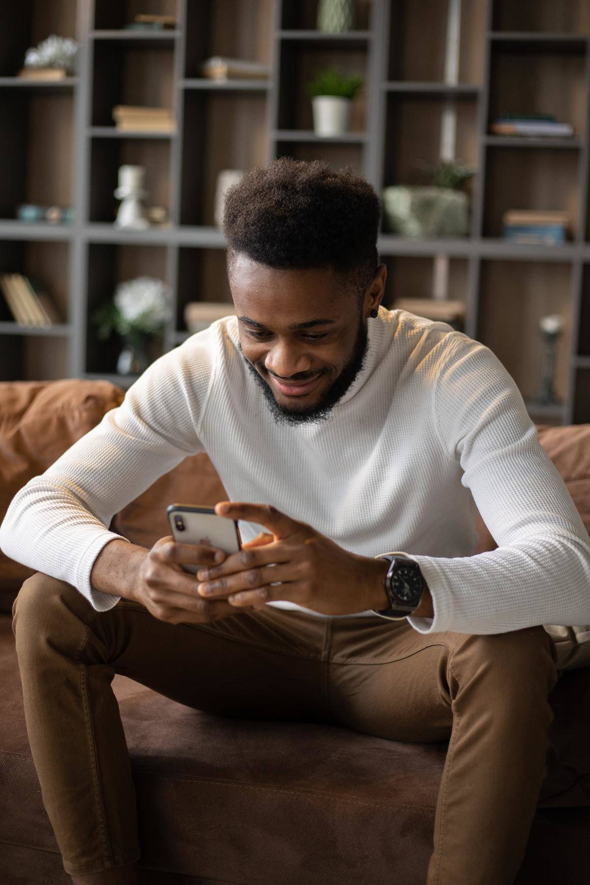 Man sitting on couch using cell phone smiling at screen