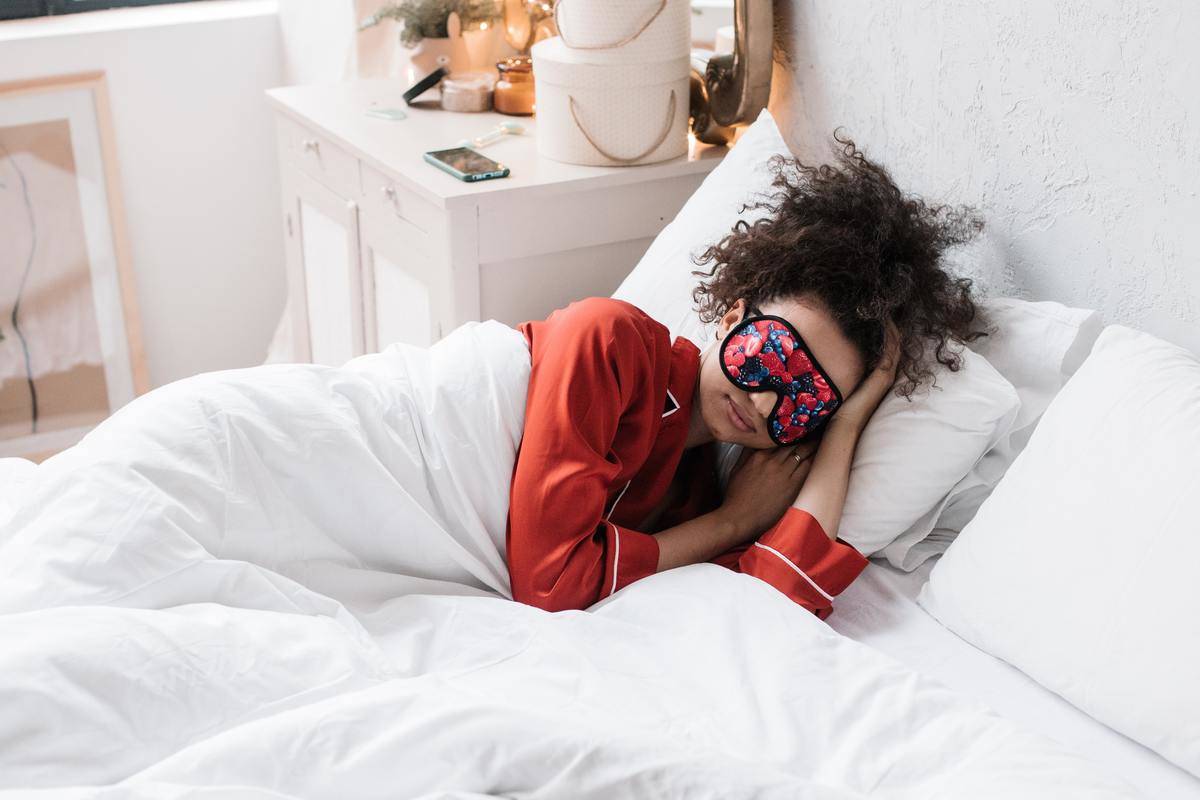 Woman sleeping alone in bed wearing eye mask