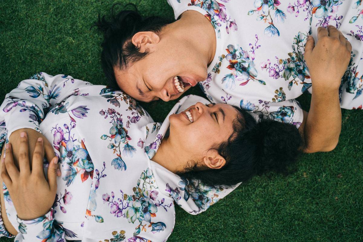 Couple wearing matching hoodies lying in grass looking at each other smiling