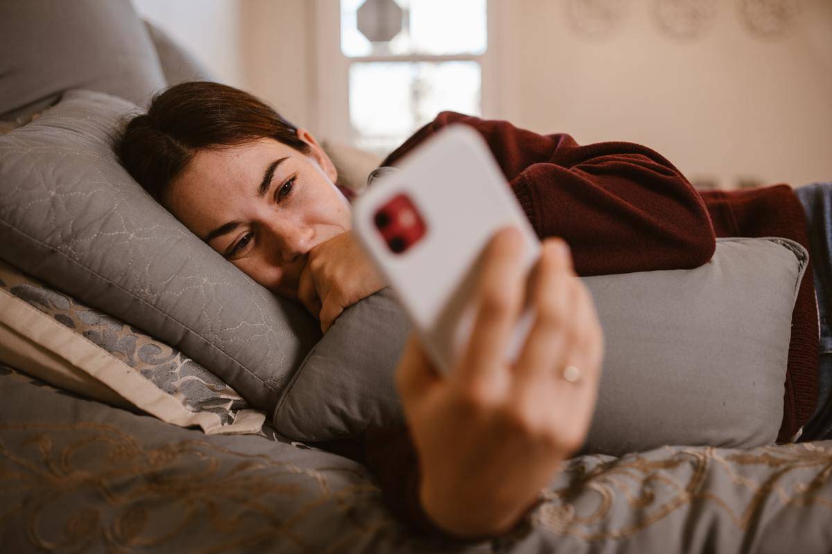 Woman looking at phone sadly while lying in bed