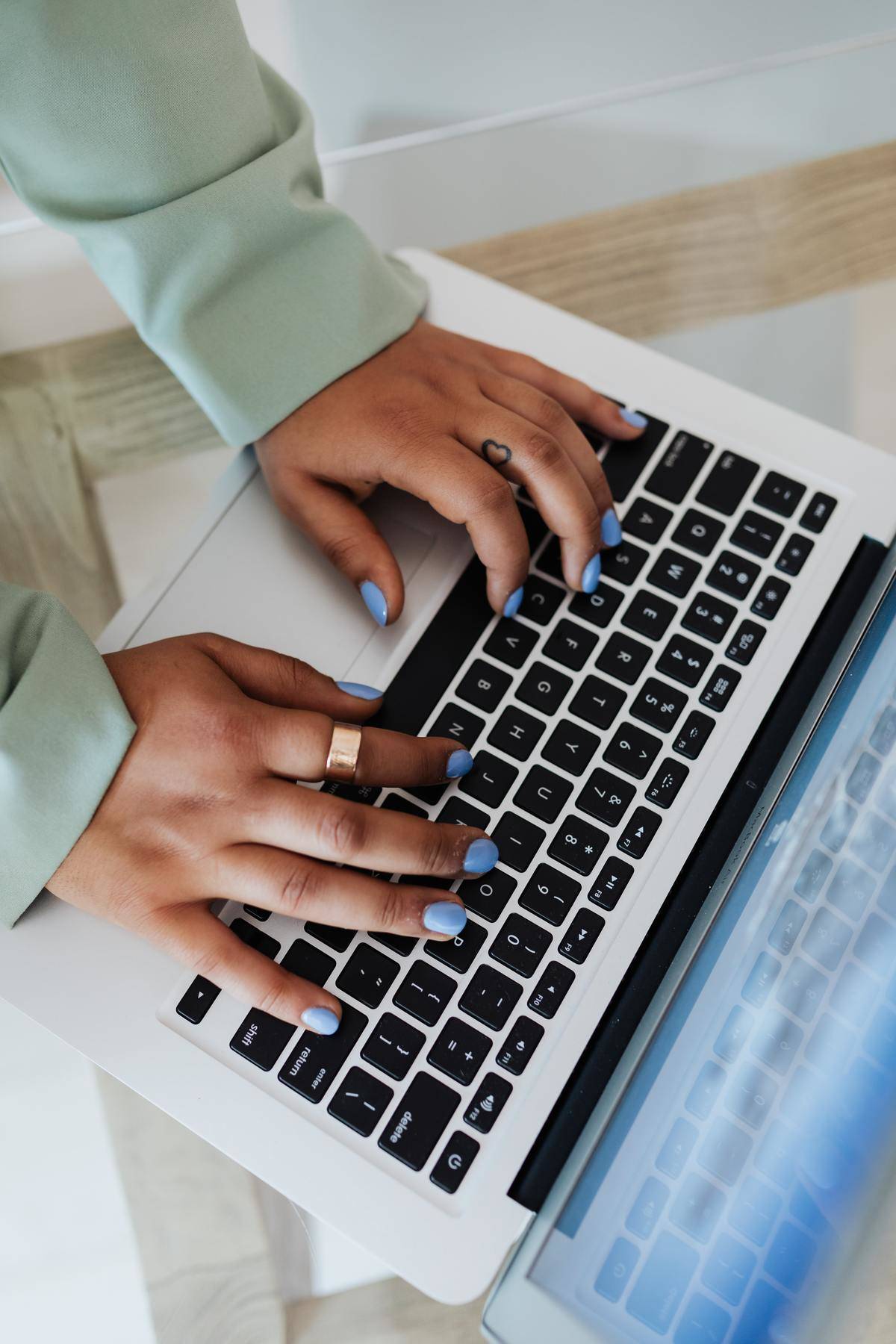 Woman wearing blue nail polish typing on laptop 