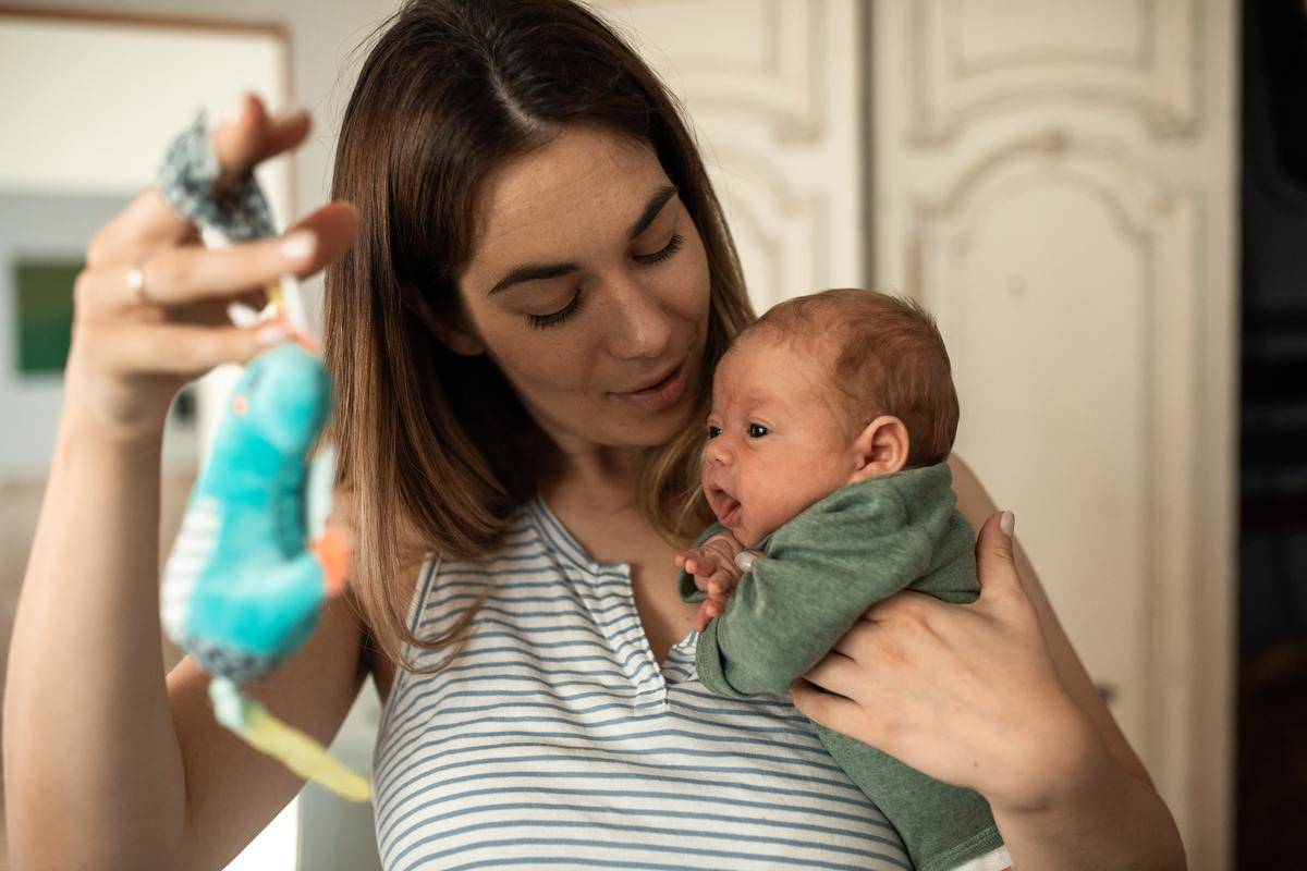 Mom looking down at new born baby holding mobile toy