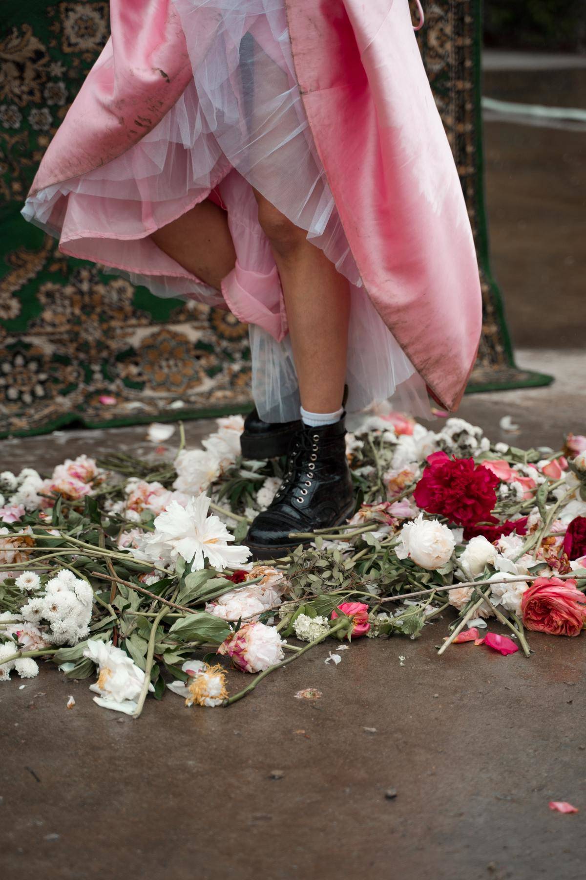 Woman wearing pink tulle dress and combat boots stepping on roses