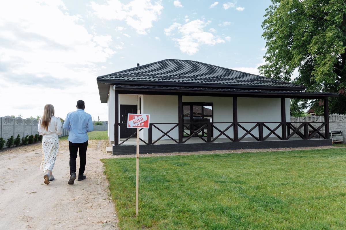 Young man and woman approaching house with SOLD online 