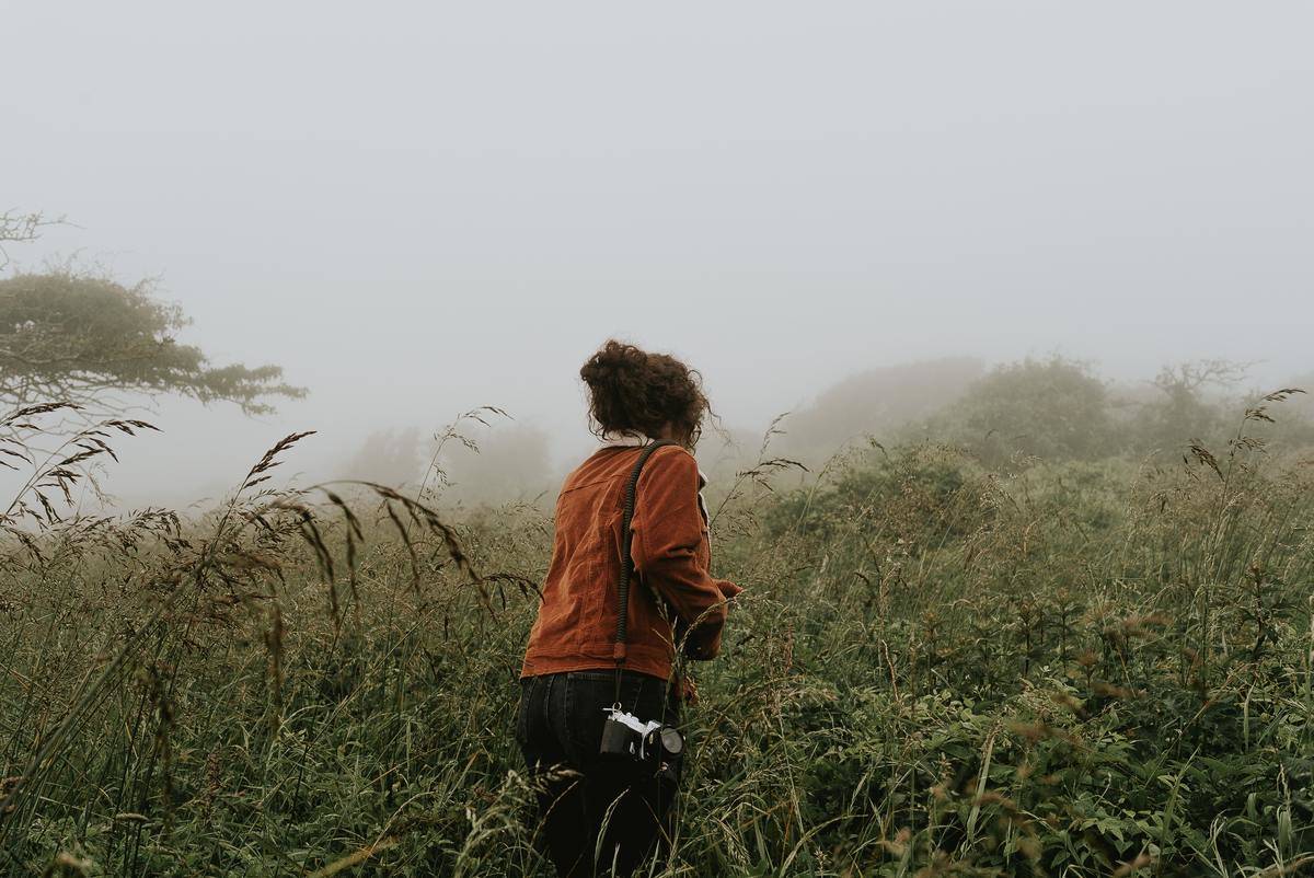 Woman walking into misty field alone with camera
