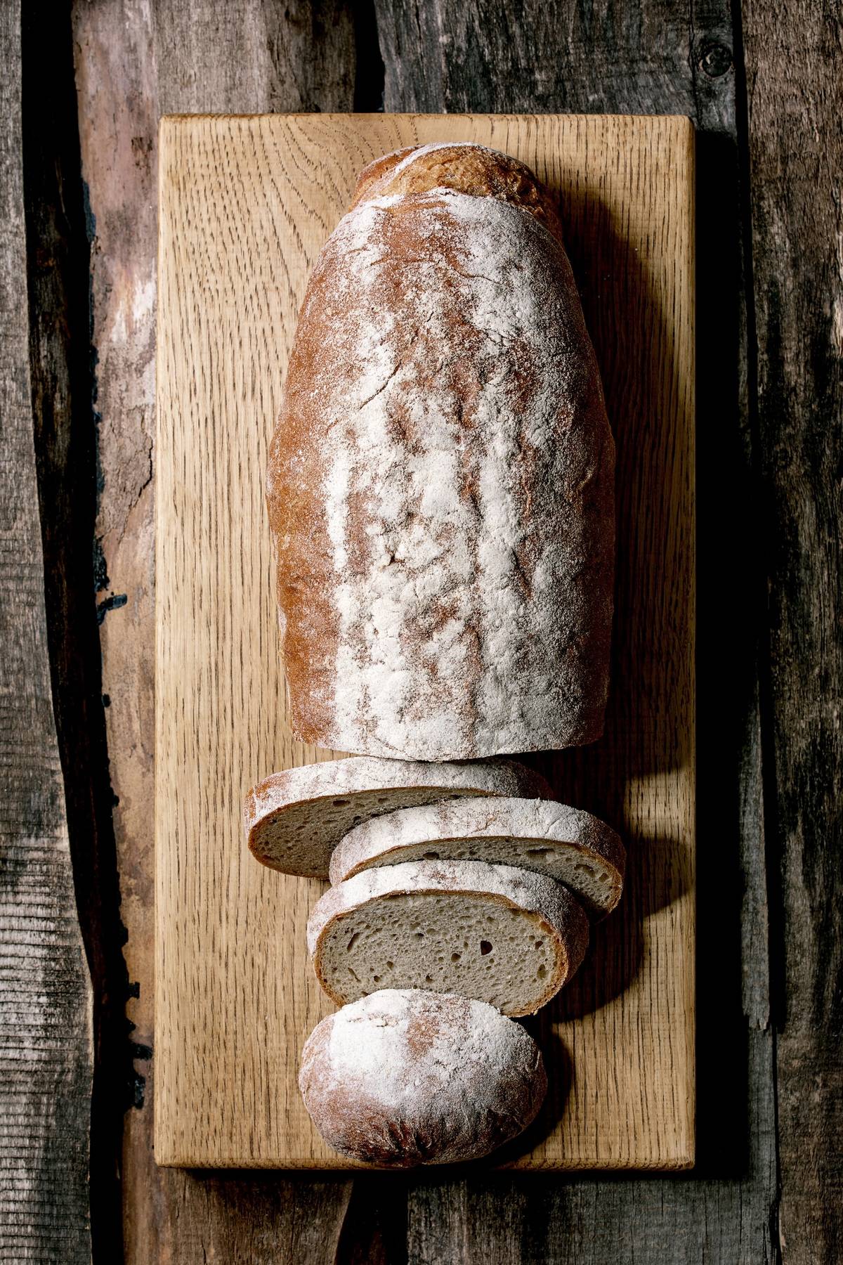 Sliced whole grain artisan rye-wheat organic bread on wood cutting board over old wooden background. Flat lay, space