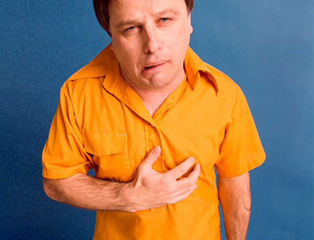 Man in bright yellow shirt holding chest with heartburn