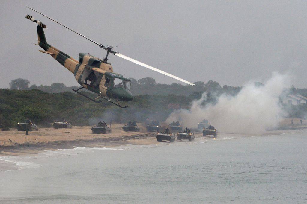 Iranian helicopter flies over beach, smoke billows in background