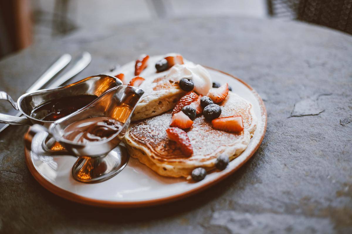 Pancake with fruit toppings and two saucers of syrup.