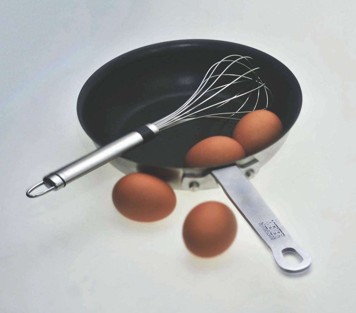 Two whole eggs in a pan with a whisk and two whole eggs outside the pan.