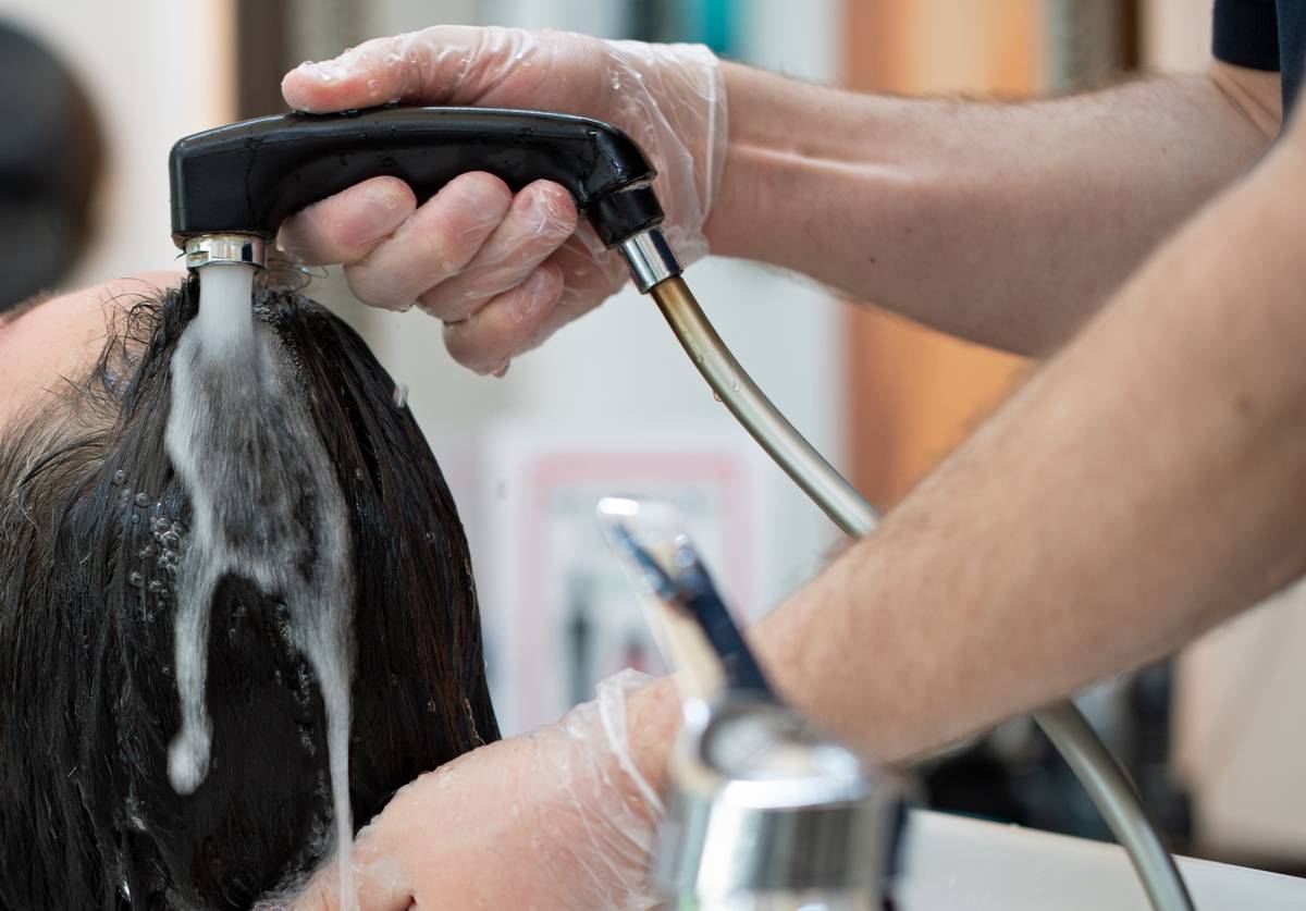 A hairdresser washes a customer's hair at a sink in a hair salon