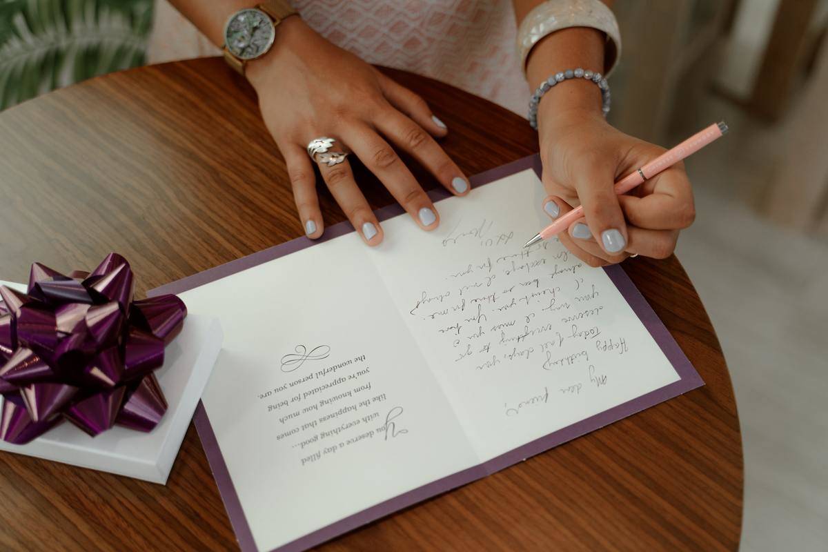 A photo of a woman writing a handwritten note on a card.