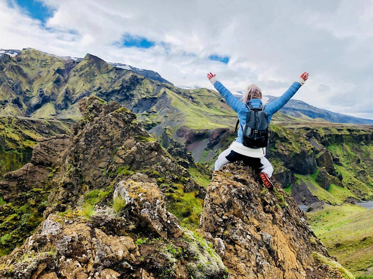 Woman raising arms in celebration while sitting on rocky mountain peak