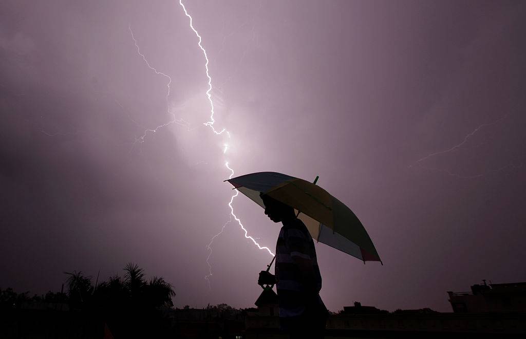 A pedestrian walks with an umbrella as lightning strikes during an evening thunderstorm