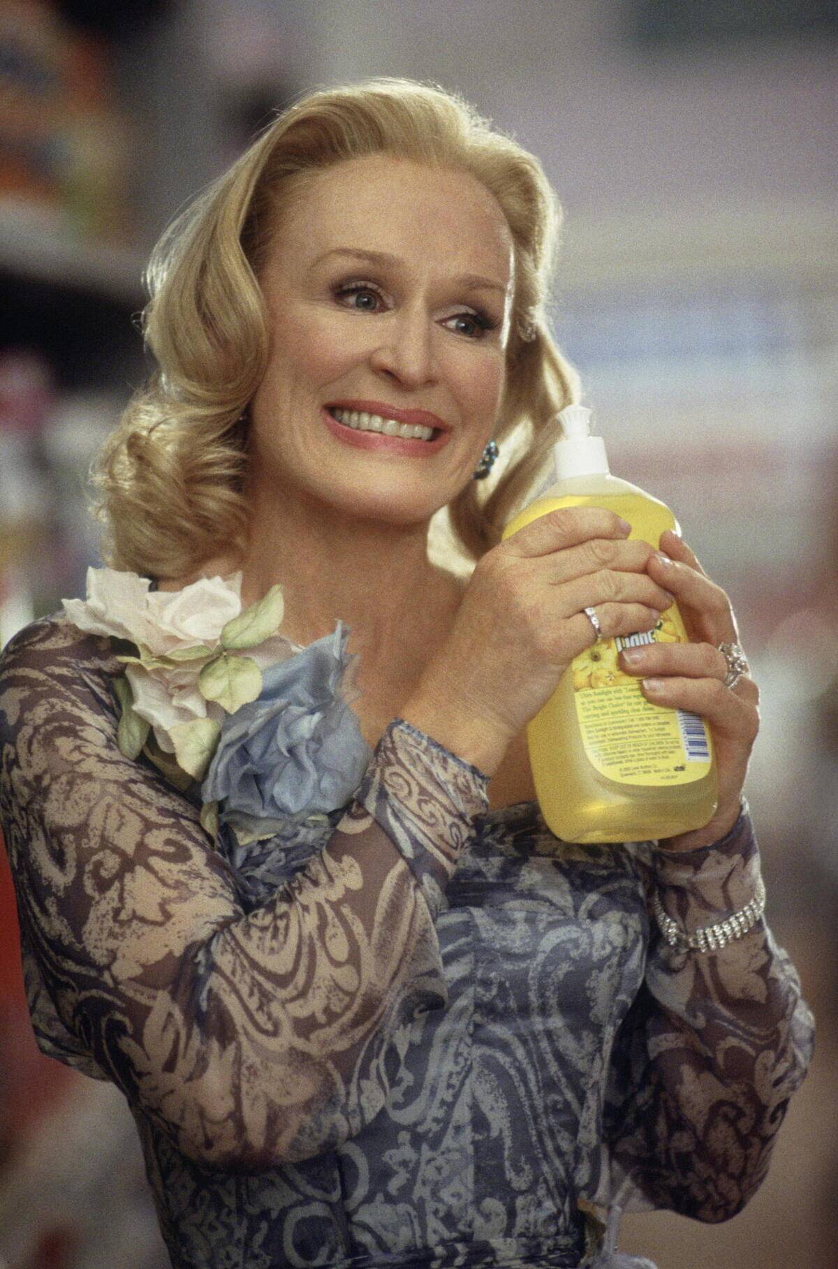 Glenn Close as Claire Wellington smiling uncomfortably while holding cleaning product in The Stepford Wives