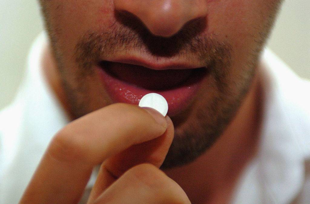 An unidentified man puts an Aspirin tablet into his mouth