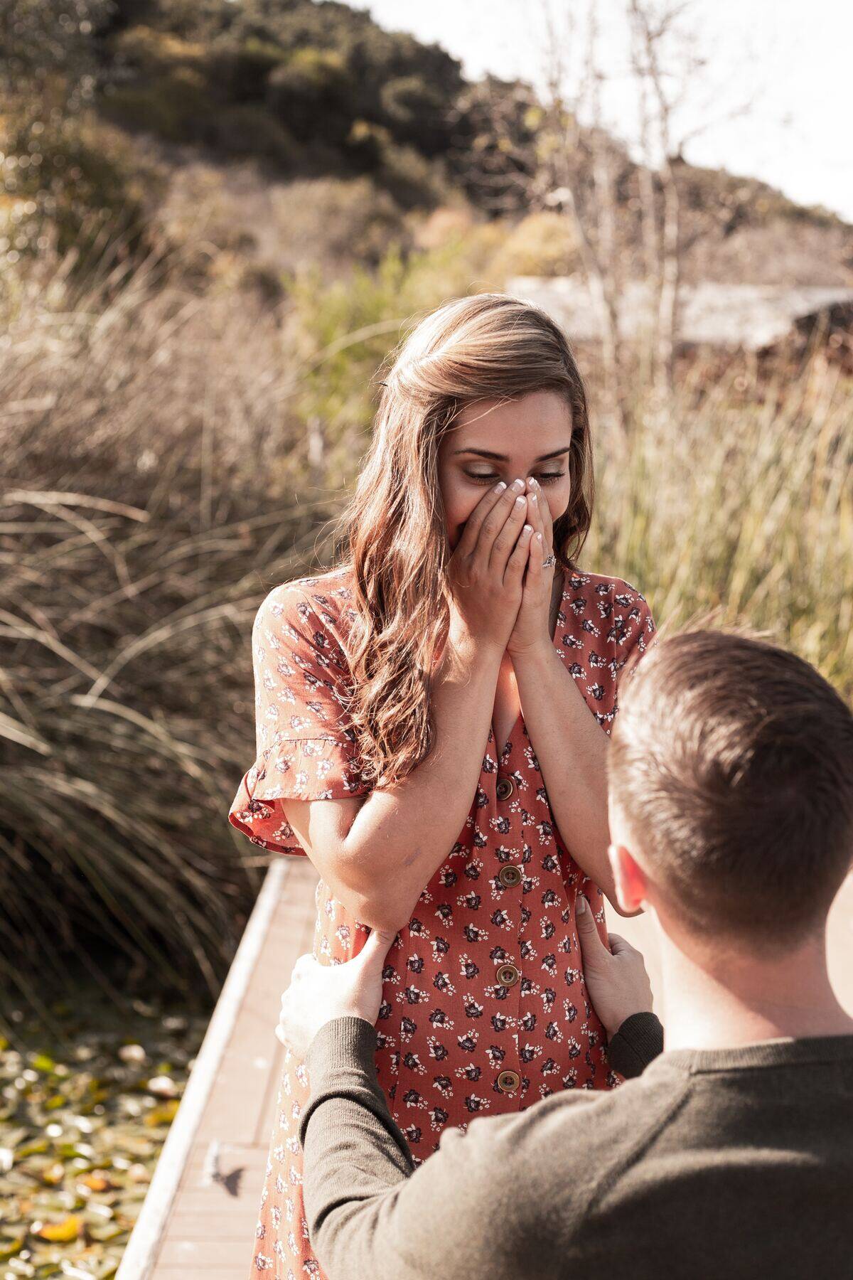 man holding woman's waist while she covers her face in amazement