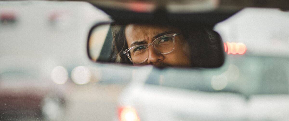 man looking into car's rear view mirror with frustrated facial expression
