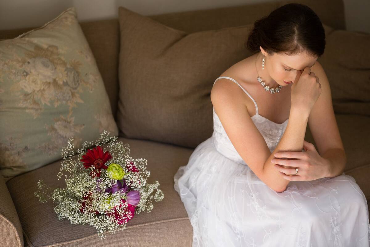 sad-bride-sitting-by-bouquet-on-sofa-at-home-2021-08-28-16-45-55-utc