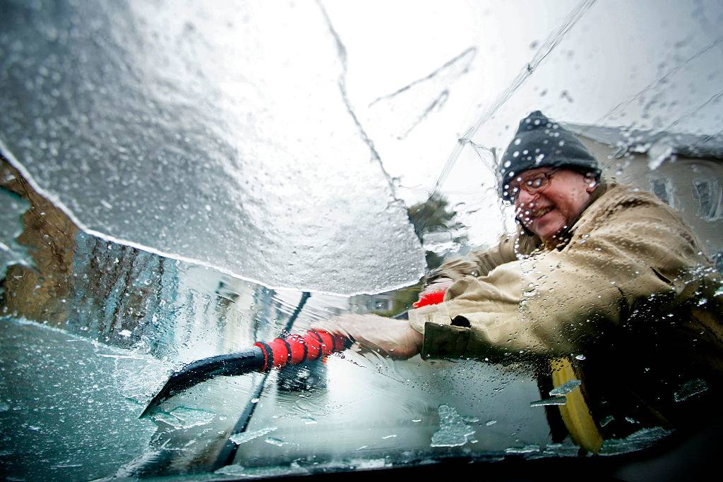 man scraping ice off his windshield