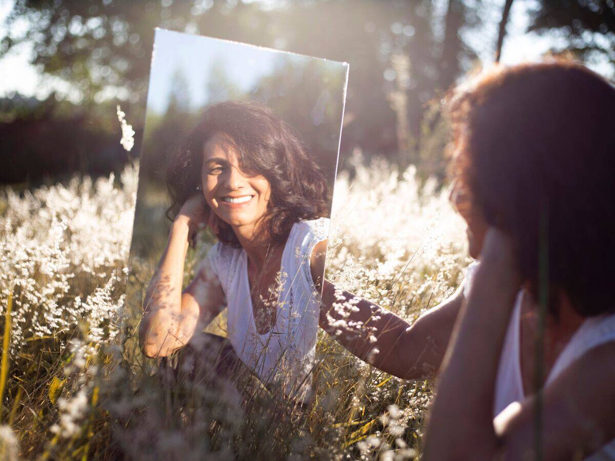 woman admiring herself in mirror among flowers
